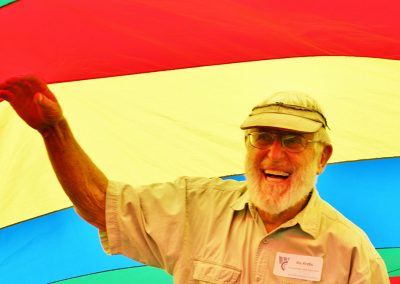 A photo portrait of Stu Krebs, laughing and holding his hand up in front of a rainbow-colored banner
