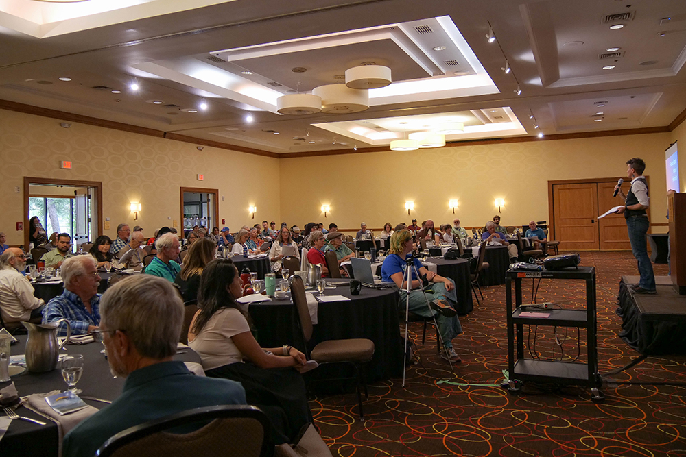 An audience of about 100 people listen to Executive Director Emily Hornback